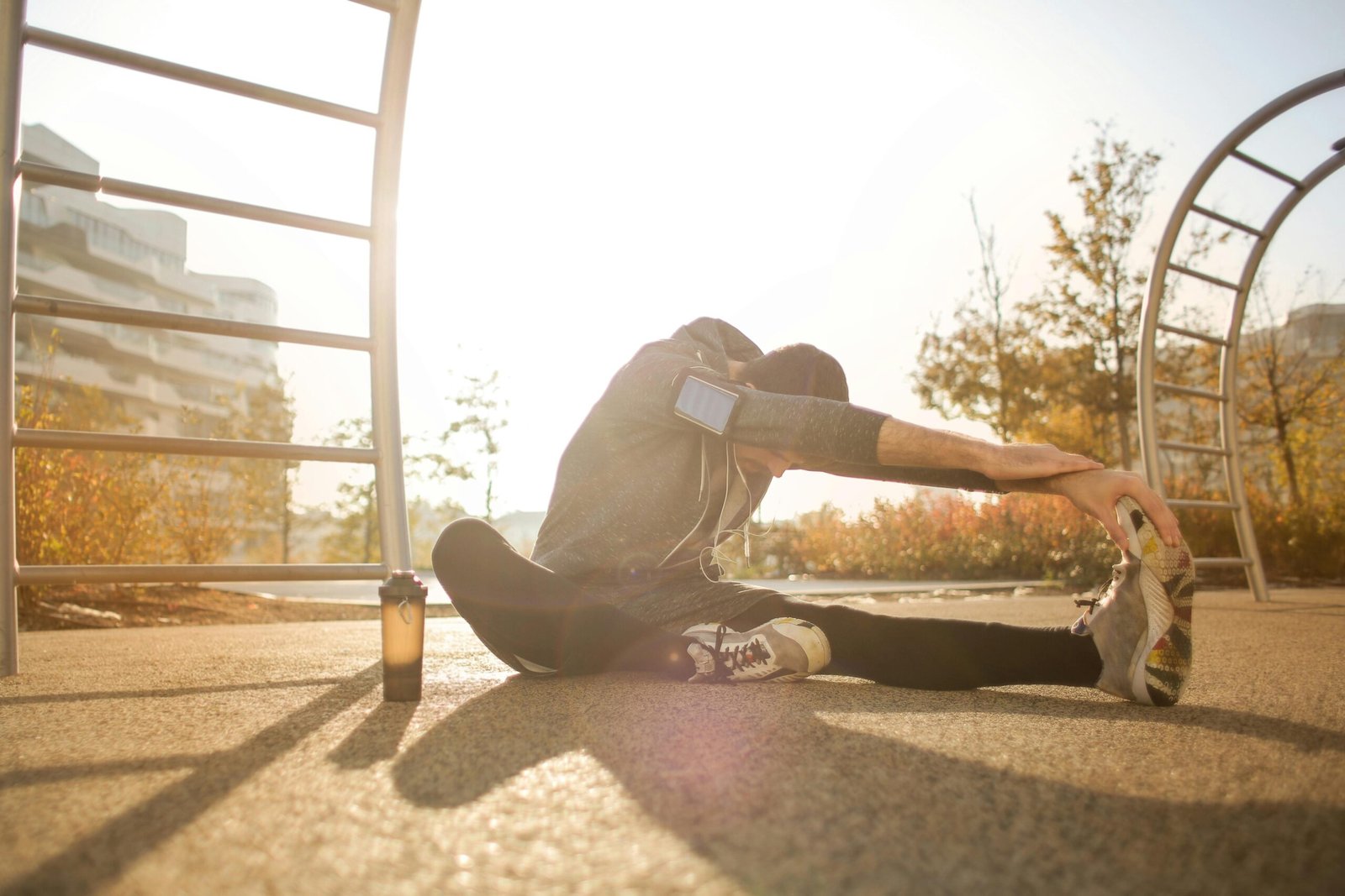 A man stretches in a park wearing activewear, focused on his fitness routine at sunrise.